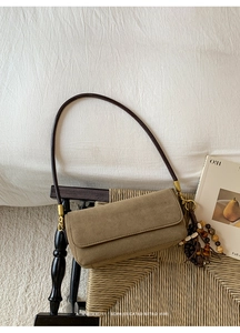 Detailed close-up of retro suede baguette shoulder bag with beaded charm on a rattan chair