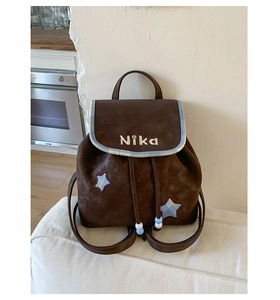 Detail of vintage brown suede backpack featuring white NiKa embroidery and star patches