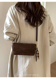 Close-up of minimalist brown suede handbag with decorative wooden bead tassel detail