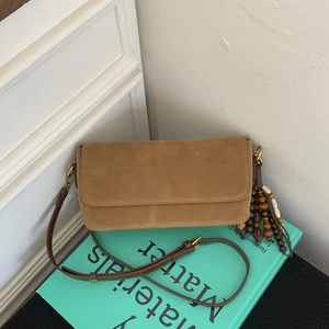 Close-up of brown suede baguette bag with colorful wooden beaded tassel on a book