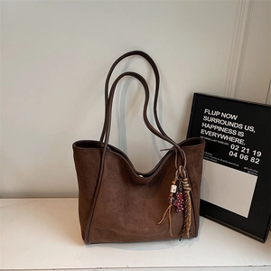 Detail of dark brown suede tote bag with creative beaded charm and slim shoulder straps