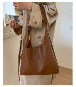 Close-up of a large vintage brown leather hobo bag worn with a chic beige trench coat