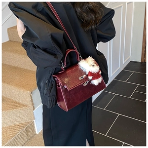 Detail view of burgundy leather handbag featuring a plush puppy charm and metallic lock