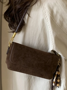 Minimalist brown suede baguette bag with tassel detail worn over a beige trench coat