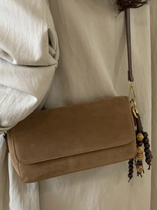 Brown suede baguette shoulder bag with decorative wooden beads on a white coat