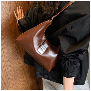 Detail van een diepbruine glanzende hobo-tas met een brede schouderband en gesp