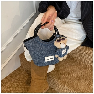 Détail d'un sac à main en denim bleu avec breloque ours en peluche et poignées noires