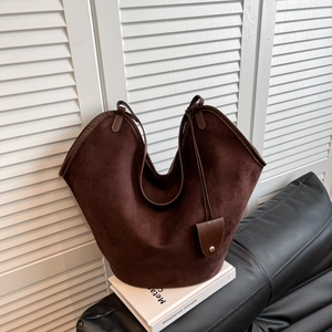 Détail macro du sac cabas en daim marron avec ouverture incurvée et breloque en métal