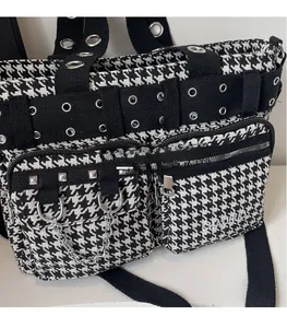 Detail of houndstooth crossbody bag with silver eyelets and metal chain accents