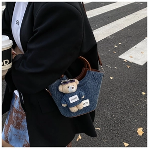 Détail du sac seau en denim bleu avec anse marron et un accessoire de charme ours en peluche