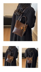 Detail of dark brown leather handbag with suede texture, gold logo, and wooden bead charm