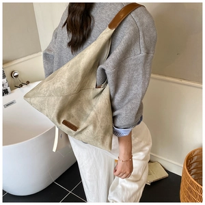 Detail of grey-green suede tote bag with brown leather strap in a minimalist setting