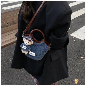 Detail view of denim bucket bag with brown leather trim and cute bear charm pendant