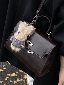 Elegant dark brown leather handbag with silver lock and plush bear on autumn background
