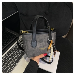 Detail of grey denim texture bucket bag with bead charm and golden text on corduroy background