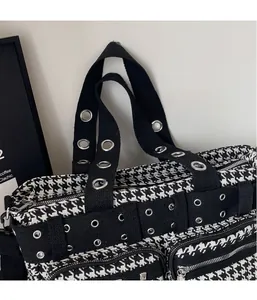 Close-up of houndstooth handbag featuring silver metal eyelet studs and side zipper detail