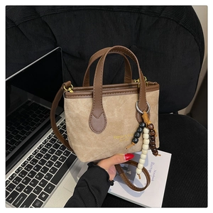 Detail of khaki bucket bag with brown trim and wooden bead charm on office desk