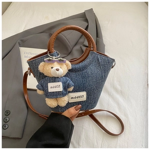 Détail du sac bandoulière en jean bleu avec anses en cuir marron et pendentif ourson