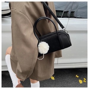 Detail of a black suede bowling bag featuring a soft white plush ball and pearl chain