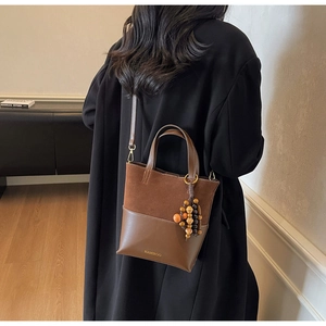 Brown suede and leather patchwork tote bag with wooden bead charm on a black wool coat