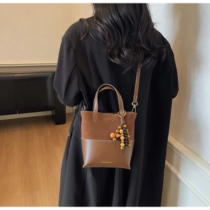 Back view of model carrying a brown patchwork leather handbag with wood bead charm