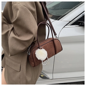 Detailed view of brown suede bowling bag with white pompom and pearl chain accessories