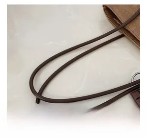 Detail view of woven tote bag showing round brown leather handles and natural fiber texture
