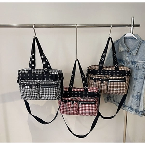 Three houndstooth messenger bags with metal eyelets and chains hanging on a rack