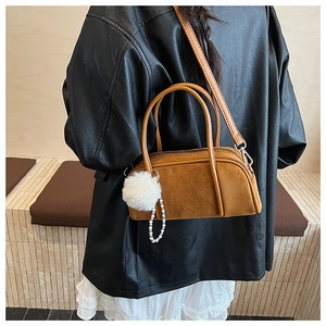 Brown suede bowling bag featuring white pompom and pearl chain on a stylish model