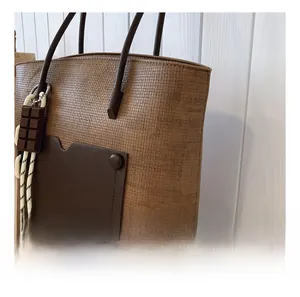 Detail of brown woven tote bag with dark leather pocket and chocolate charm accessory
