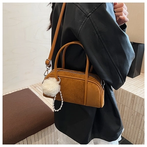 Close-up of brown suede Boston bag featuring pearl chain and white fuzzy pom-pom charm