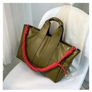 Detail of olive green tote bag featuring distinctive red braided rope shoulder straps