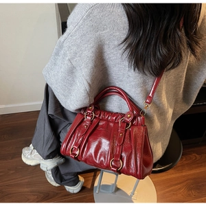 Detail of burgundy glossy pleated baguette bag with gold metal hardware and strap