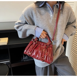 Detail of dark red pleated handbag with golden rings and glossy leather finish