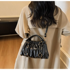 Detailed view of a black pleated baguette bag worn over a classic khaki trench coat