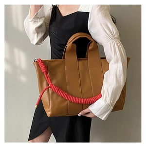 Close-up of caramel tote bag with red rope woven strap and matte leather texture