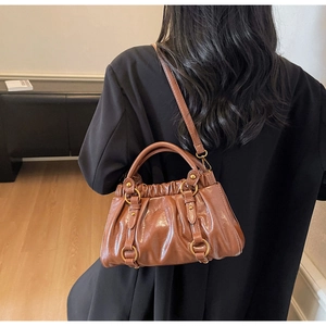 Detail of a brown pleated dumpling bag showing the glossy leather texture and gold hardware