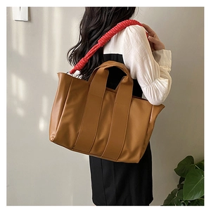 Detail of a large brown tote bag with a unique red spiral shoulder strap and top handles