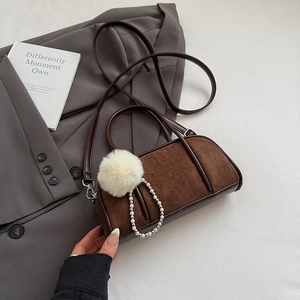Detail of a brown suede bowling bag with fluffy pom-poms and pearl chain accessories