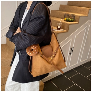 Macro detail of brown suede tote bag featuring a leather buckle and a donut plush charm