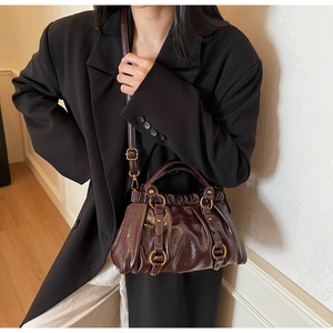 Detail view of brown glossy leather bag with gold buckle on a model in a black suit