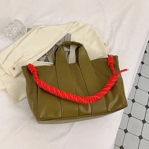 Close-up of olive green tote bag featuring a red braided rope strap on a flat lay set