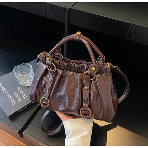 Detailed macro view of dark brown pleated leather handbag with gold metal ring buckles