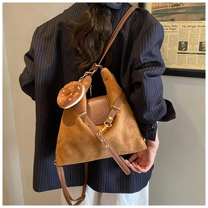 Detail of brown suede crossbody bag with donut plush charm on a model in striped blazer