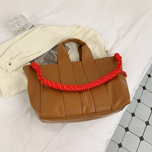 Detail of caramel tote bag with thick red and white woven rope handles on a soft surface