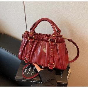 Detail view of burgundy pleated leather handbag with gold ring hardware and rivets