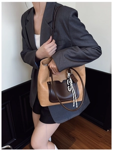 Model wearing a large camel straw-textured tote bag with dark brown leather pocket and strap
