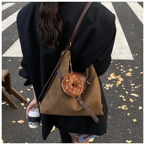 Close-up of brown suede hobo bag with leather strap and cute donut charm on urban street