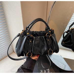 Close-up of black pleated dumpling bag with glossy finish and golden metal ring detail