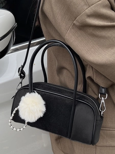 Elegant black suede bowling bag with white fur ball and pearl pendant shown in a street setting